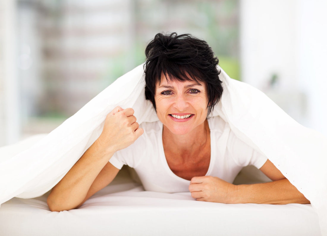 middle_aged_women_looking_up_smiling_under_bed_covers